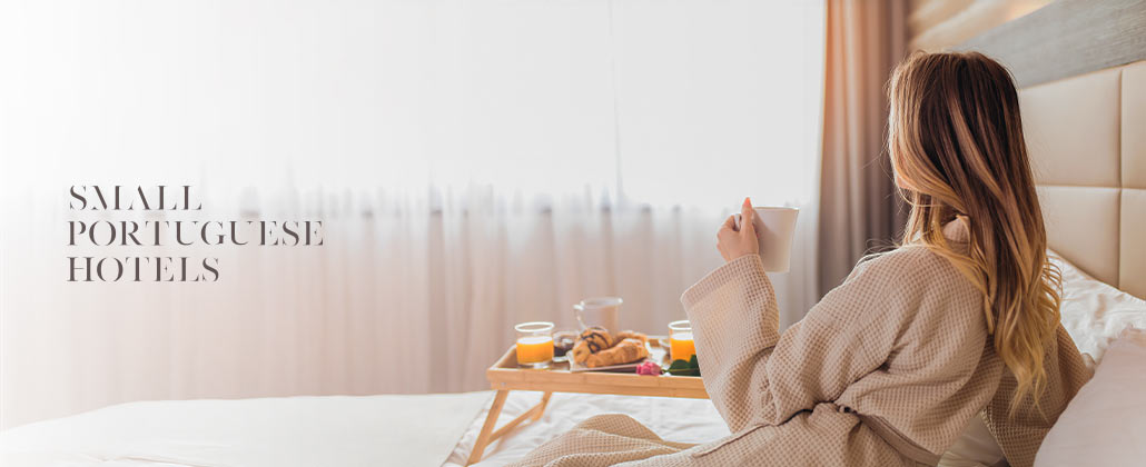 Mulher a relaxar numa cama de hotel, enquanto toma o pequeno-almoço